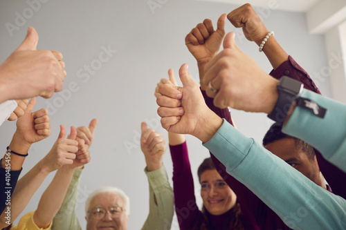 Well done. Group of happy smiling diverse people raising hands and giving thumbs-up, celebrating successful teamwork and excellent results, demonstrating positive attitude and strong team spirit photo