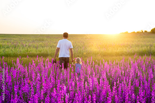 Dad and daughter walking towards the sun across a lavender purple field. Parent-child relationships, joint walks, an active lifestyle.
