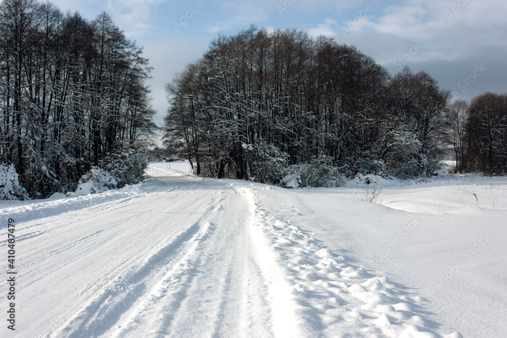 Suburbs of Grodno. Belarus. Winter landscape outside the city. Snow-covered field after heavy snowfall and a cleared road, trees in the snow, blue sky.