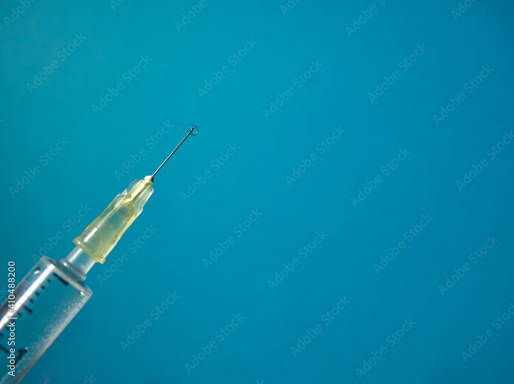 A syringe with liquid drop on blue background A syringe with liquid drop on blue background