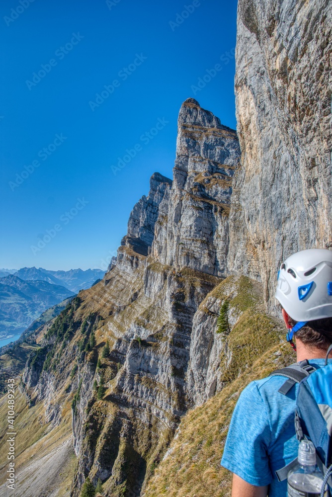 men with backpack and helmet stands at steep face in the swiss mountains during hike men with backpack and helmet stands at steep face in the swiss mountains during hike