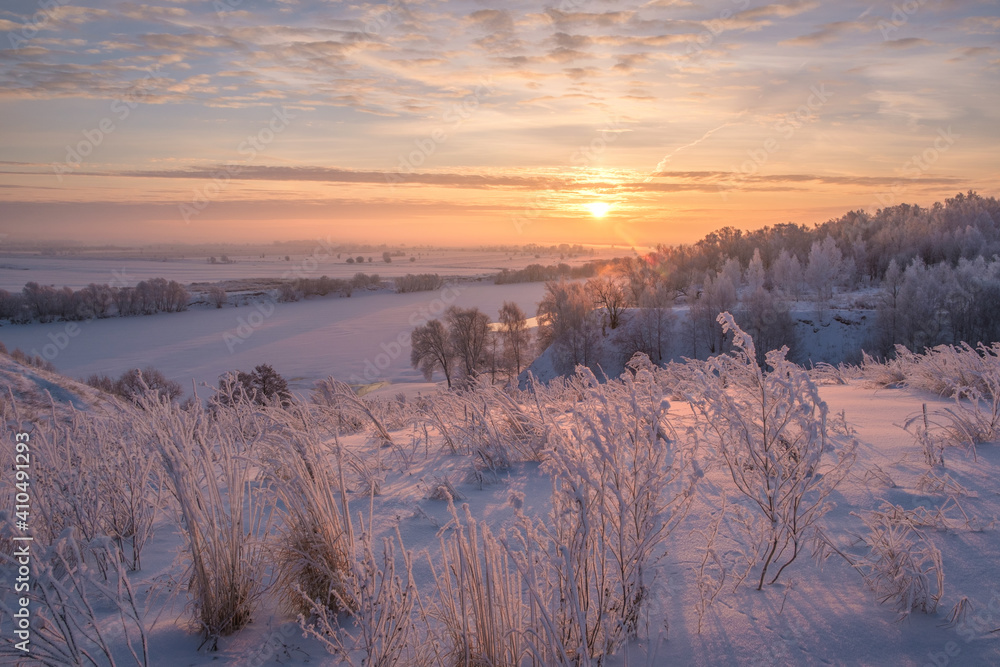 Beautiful winter landscape. Sunrise over the river. Snow-covered trees on the banks of the river.