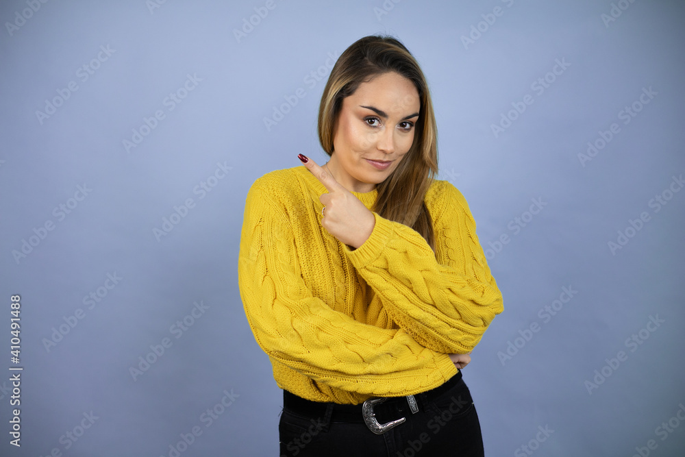 Fototapeta premium Young beautiful blonde woman with long hair wearing a yellow sweater surprised pointing with hand and finger to the side