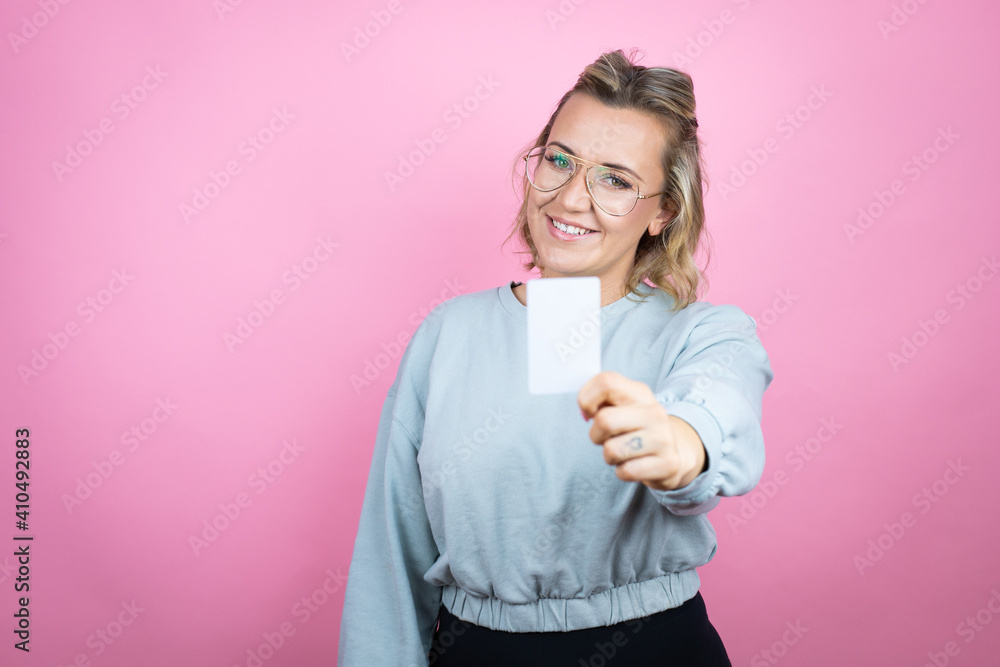 Young caucasian woman wearing sweatshirt over pink background smiling and holding white card Young caucasian woman wearing sweatshirt over pink background smiling and holding white card