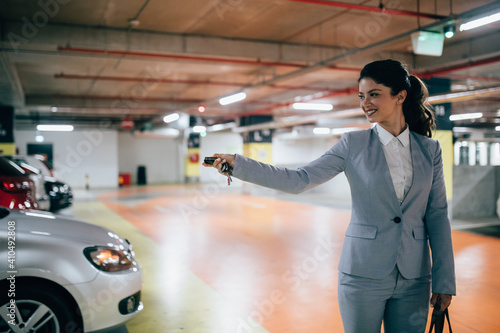 Elegant businesswoman locking her car with keys in underground parking.