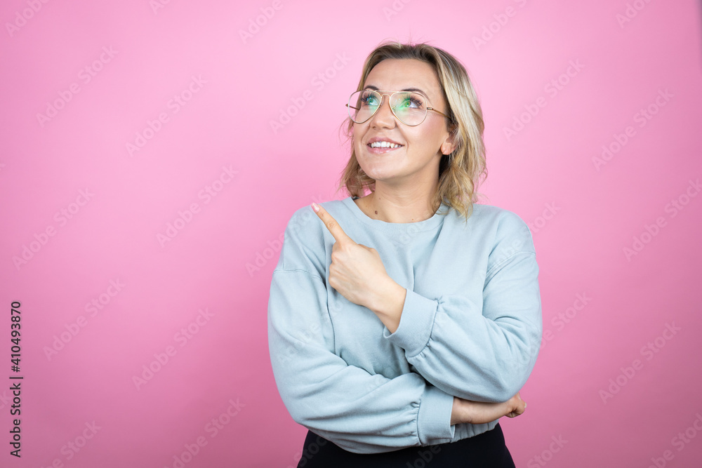 Young caucasian woman wearing sweatshirt over pink background confused and pointing with hand and finger to the side Young caucasian woman wearing sweatshirt over pink background confused and pointing with hand and finger to the side