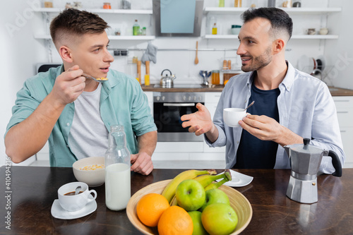 happy man gesturing while looking at husband during breakfast