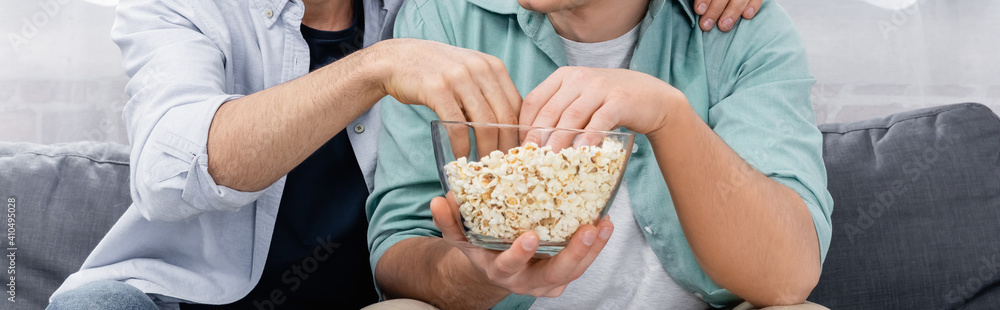 partial view of same sex couple watching movie with popcorn, banner partial view of same sex couple watching movie with popcorn, banner
