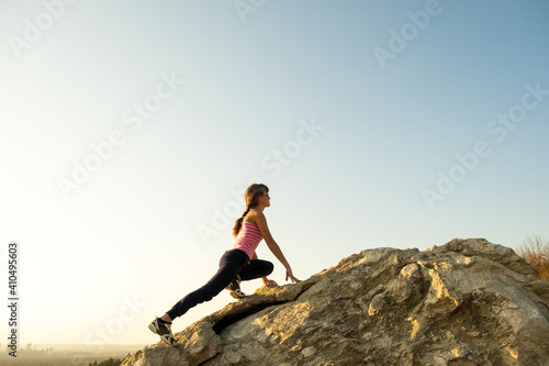 Woman hiker climbing steep big rock on a sunny day. Young female climber overcomes difficult climbing route. Active recreation in nature concept.