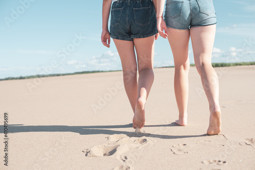 Image of female feet close-up on a beach background. Two women walk barefoot on the sand, leaving footprints. © mavrik