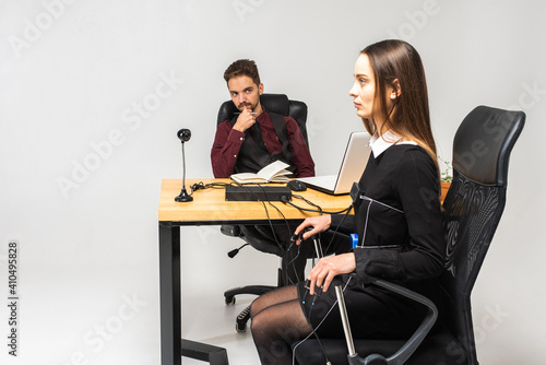 Concentrated, thoughtful woman is in a bright room, testing on a computer polygraph. Young man sitting at the table and looking at the polygraph screen and polygraph monitoring. The concept of truth