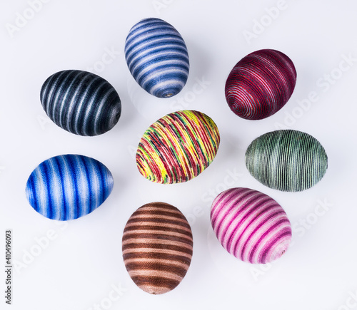 Group of colored Easter eggs with striped pattern on a white background. Collection of hollow shells hand-decorated by pasted sewing cotton yarn. Set of various streaked holiday decorations. Top view.