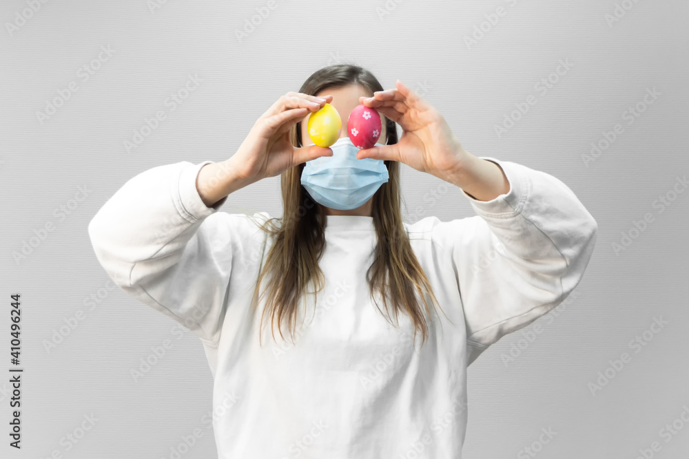 Woman with Easter eggs on eyes and medical mask on face. Easter during the coronavirus pandemic. Safety at Easter 2021 in quarantine. Woman with Easter eggs on eyes and medical mask on face. Easter during the coronavirus pandemic. Safety at Easter 2021 in quarantine.