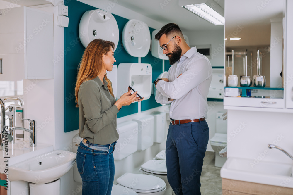 Middle age man choosing ceramic tiles and utensils for his home bathroom and female seller helps him to make right decision Middle age man choosing ceramic tiles and utensils for his home bathroom and female seller helps him to make right decision