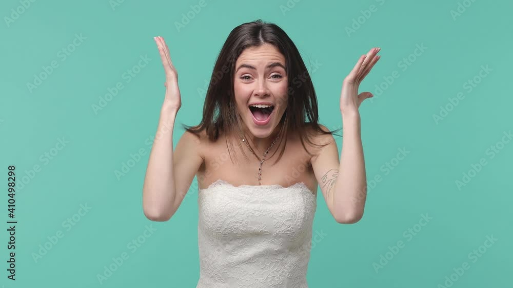 Shocked surprised amazed bride young woman 20s in beautiful white wedding dress posing isolated on blue turquoise wall background studio. Wedding concept. Say wow cover mouth with hands spreading arms Shocked surprised amazed bride young woman 20s in beautiful white wedding dress posing isolated on blue turquoise wall background studio. Wedding concept. Say wow cover mouth with hands spreading arms