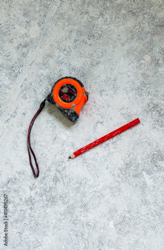 Vibrant orange tape measure and red pencil on the dirty dusty concrete floor in the renovated room in new apartment or building 