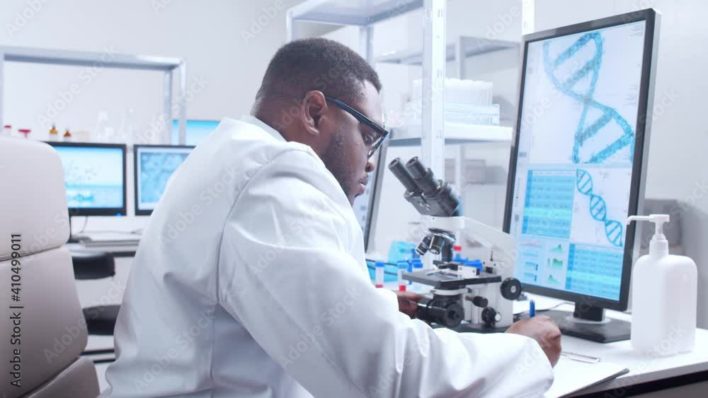 Professional African-American scientist is working on a vaccine in a modern scientific research laboratory. Genetic engineer workplace. Futuristic technology and science concept. Professional African-American scientist is working on a vaccine in a modern scientific research laboratory. Genetic engineer workplace. Futuristic technology and science concept.
