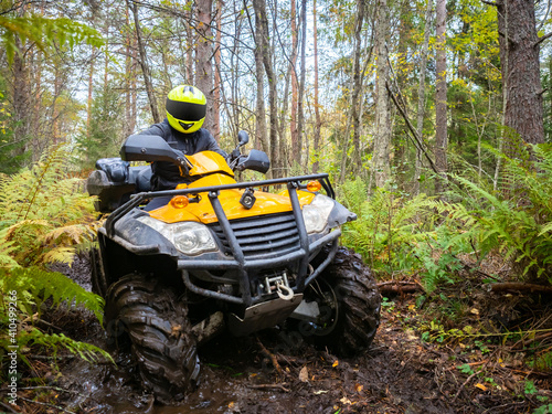 ATV racing in the woods. Extreme ATV racing off-road. Biker's journey in woods. Biker on a yellow ATV. Portrait of a biker in mud. Motocross in the green taiga. Participation in motocross