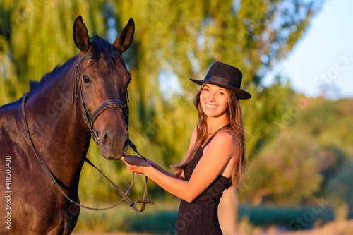 Happy girl in a hat and a horse in the rays of the warm setting sun looked into the frame