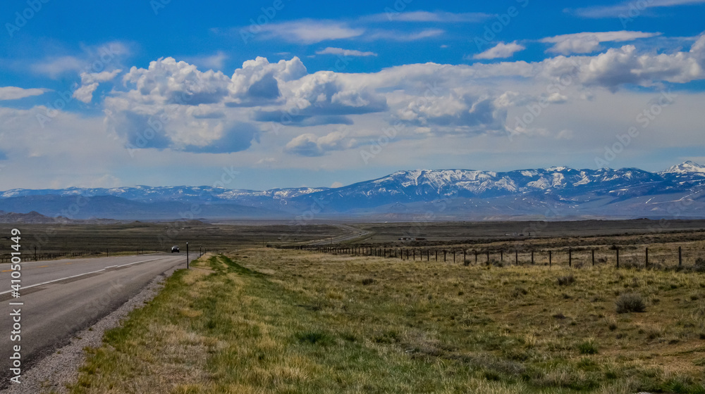 The landscape is in the wild. A road going into the distance, white clouds on the horizon.