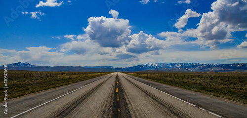 The landscape is in the wild. A road going into the distance, white clouds on the horizon.