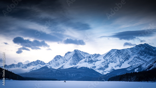 Distant fishermen stand in the middle of the frozen Kananaskis Lake surrounded by the Canadian Rocky Mountains in Alberta Canada.