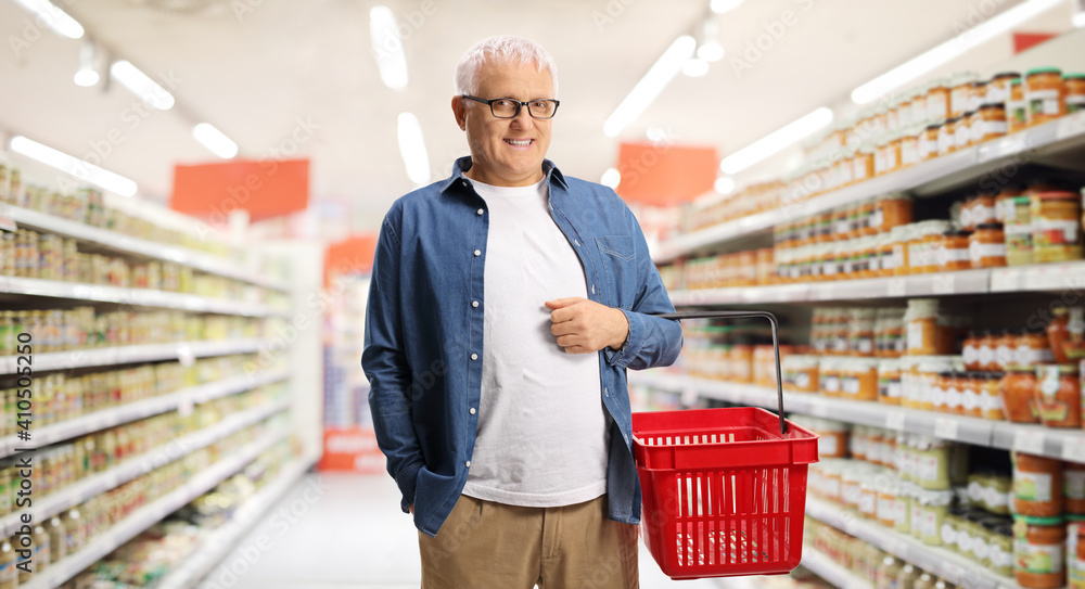 Man inside a supermarket carrying a red plastic shopping basket