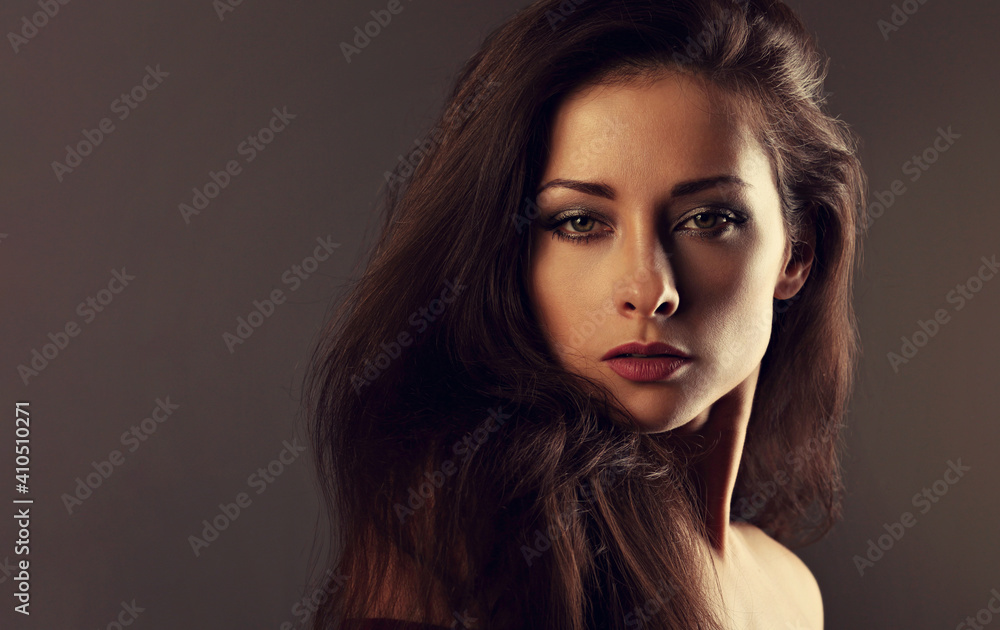 Fototapeta premium Beautiful mysterious woman makeup face and healthy volume brown hair with wisdom emotional look on brown color background with empty copy space. Closeup