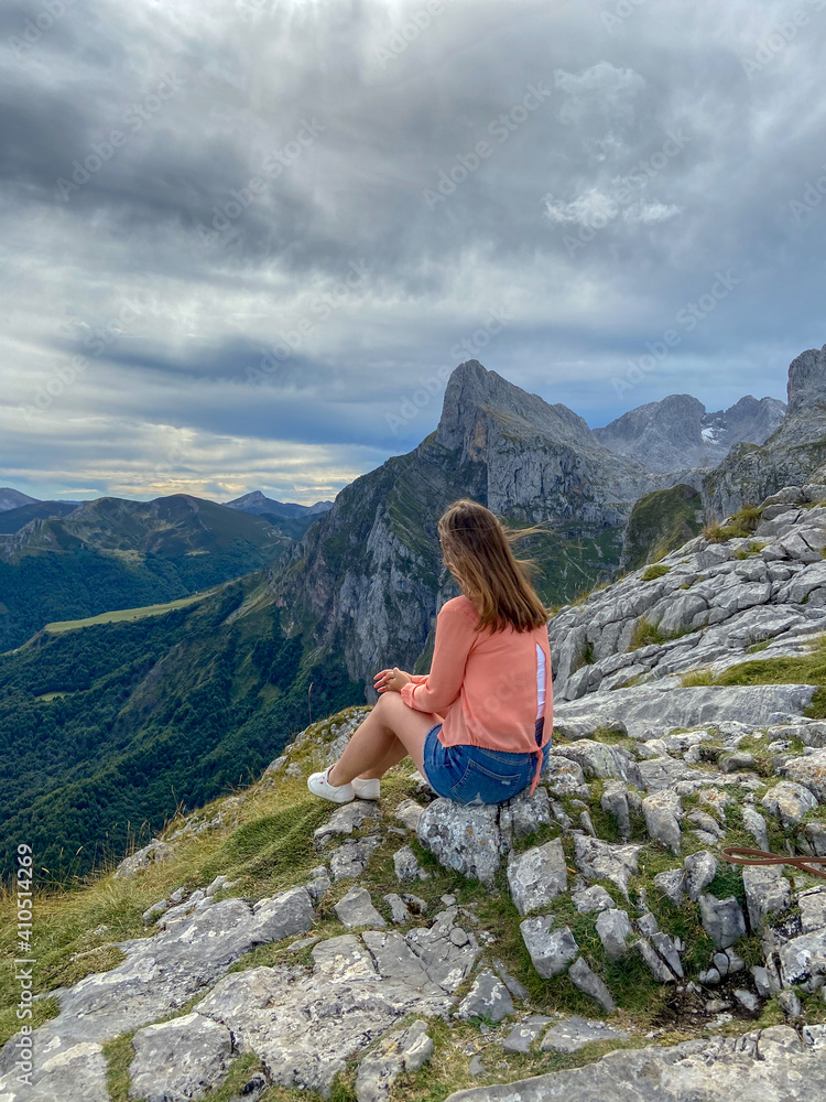 Beautiful young woman sitting next to the Majestic mountains of the Eastern Massif of the Picos de Europa. Eagles flying over Pena Remona.