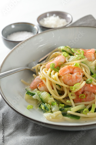Spaghetti , shrimps, zucchini and spring onions, a healthy Mediterranean meal in a grey plate with a fork, napkin and spice bowls, vertical close up shot, selected focus
