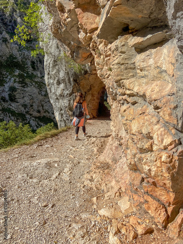 Cain, Spain - September 1, 2020: Female hiking trough the Cares Route in the heart of Picos de Europa National Park, Spain. Narrow and impressive canyon between cliffs, bridges and footpaths.