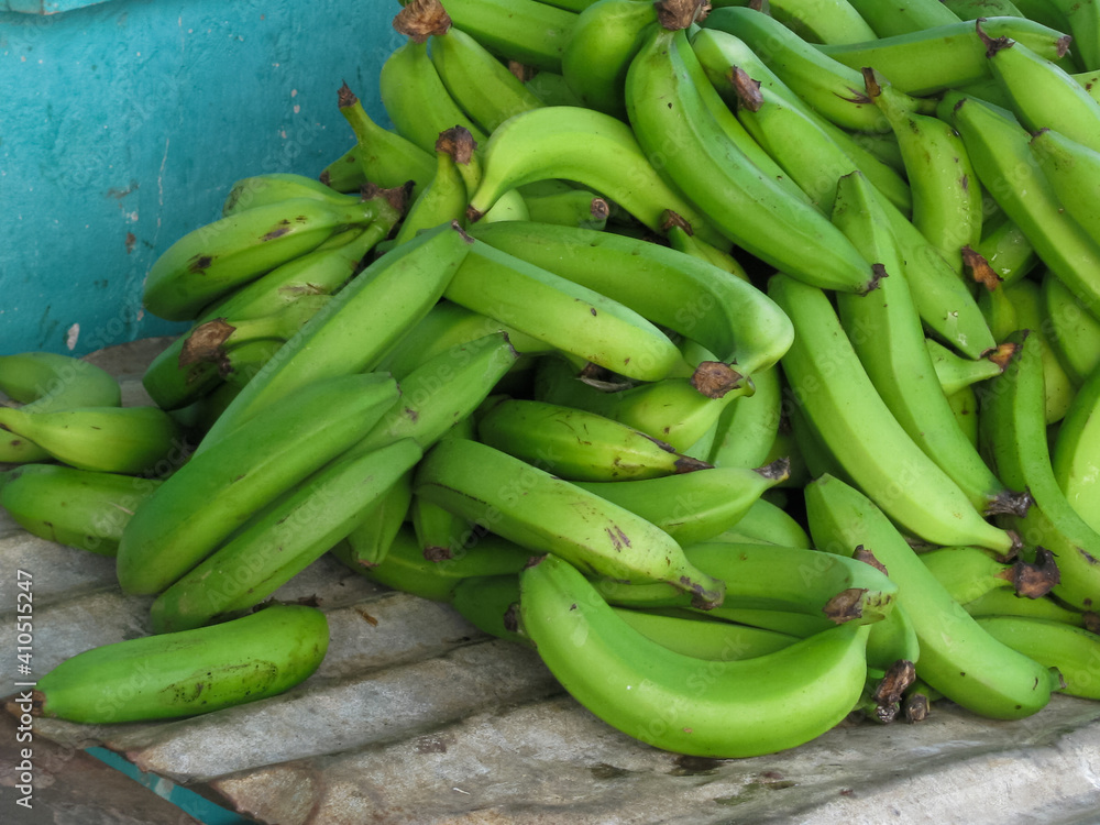 pile of bright organic green bananas at tropical local farmers market with metal and blue background