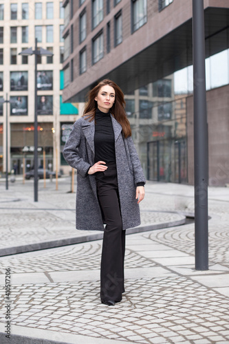beautiful girl with makeup in a spring coat and trousers posing on the city streets