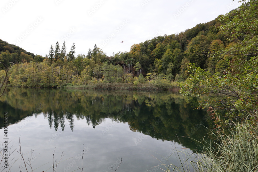 Picturesque autumn lake landscape and reflection of calm water of tree crowns and gray sky, Plitvice Lakes National Park