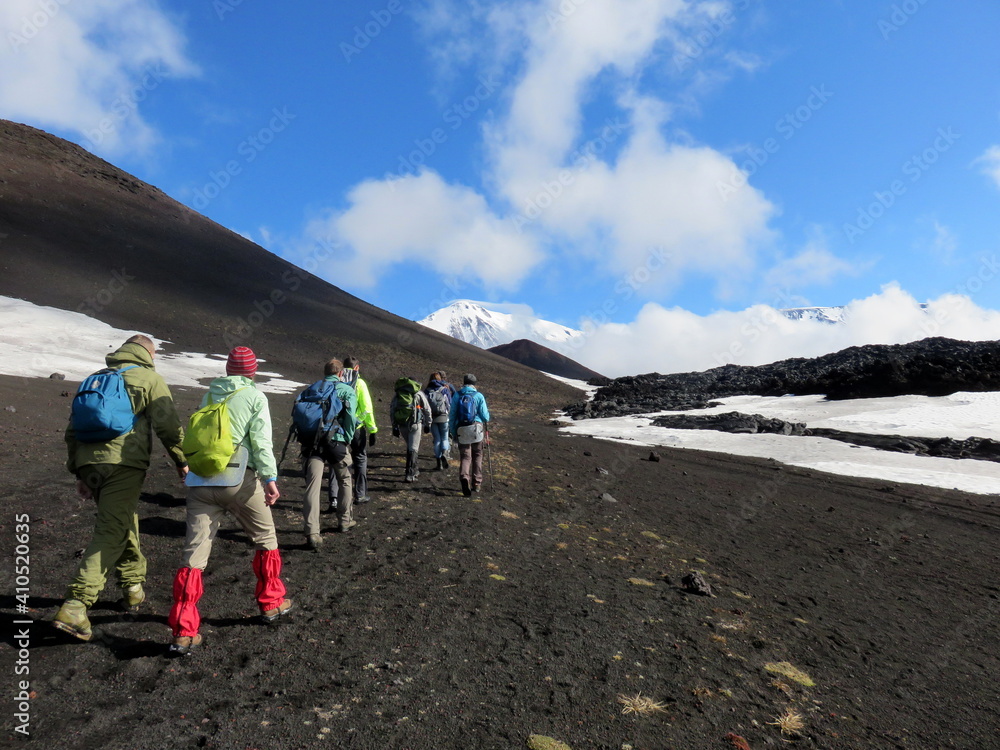 A group of hikers on black ash next to a lava field and snow in in Kamchatka, Russia