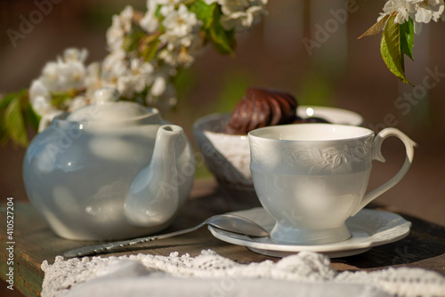 tea set, white tablecloth on a sunny day, cherry blossom branches, marshmallows in chocolate, wooden table. Outdoor breakfast, picnic, brunch, spring mood. Soft focus