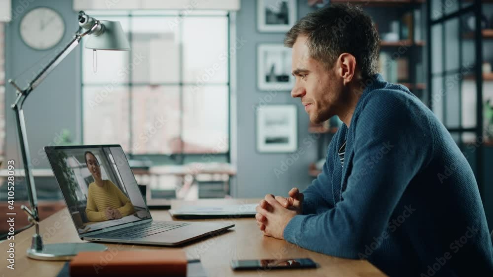 Handsome Caucasian Man Having a Video Call on Laptop Computer while Sitting Behind Desk in Living Room. Freelancer Working From Home and Talking to Colleagues and Clients Over the Internet. Handsome Caucasian Man Having a Video Call on Laptop Computer while Sitting Behind Desk in Living Room. Freelancer Working From Home and Talking to Colleagues and Clients Over the Internet.