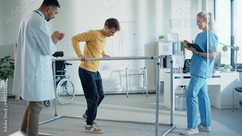 Hospital Physical Therapy: Strong Patient with Back Injury Making First Slow Steps, Walks Holding for Parallel Bars. Physiotherapist, Rehabilitation Doctor Assist, Help, Encourage Disabled Person photo