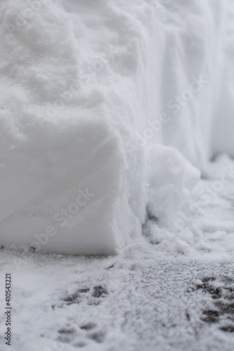 Closeup of corner of snow drift; path shoveled in snow with dog footprints 