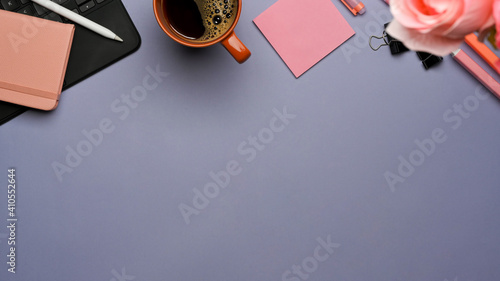 Workspace with tablet keyboard, stationery, coffee cup, flower and copy space on purple table
