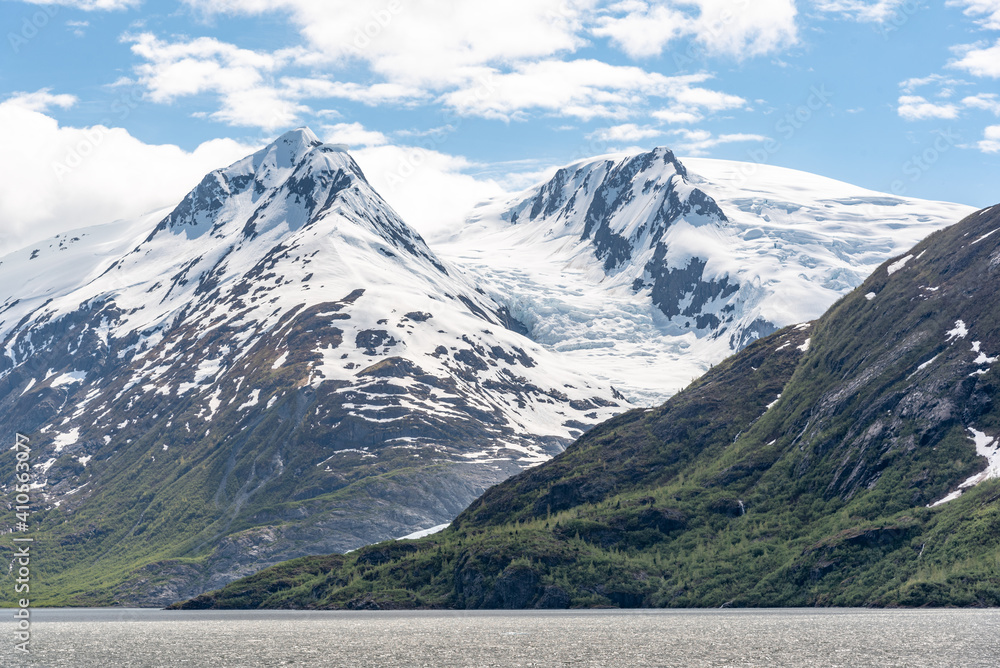Stunning, crisp and perfect summertime snow-capped mountains in Alaska with clouds covering a partially blue sky. Taken in June, summer season. 