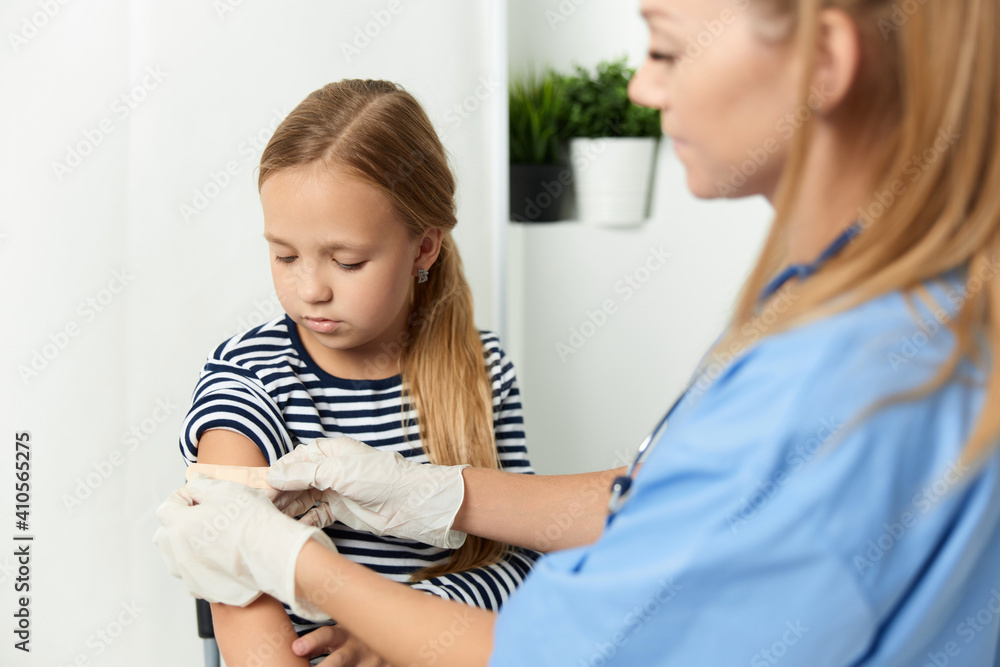 Fototapeta premium a woman doctor next to a girl seals her hand with a health adhesive