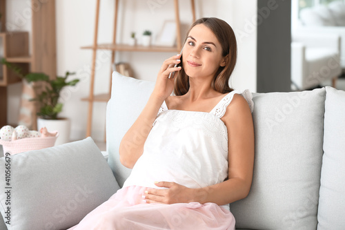 Beautiful pregnant woman talking by mobile phone at home