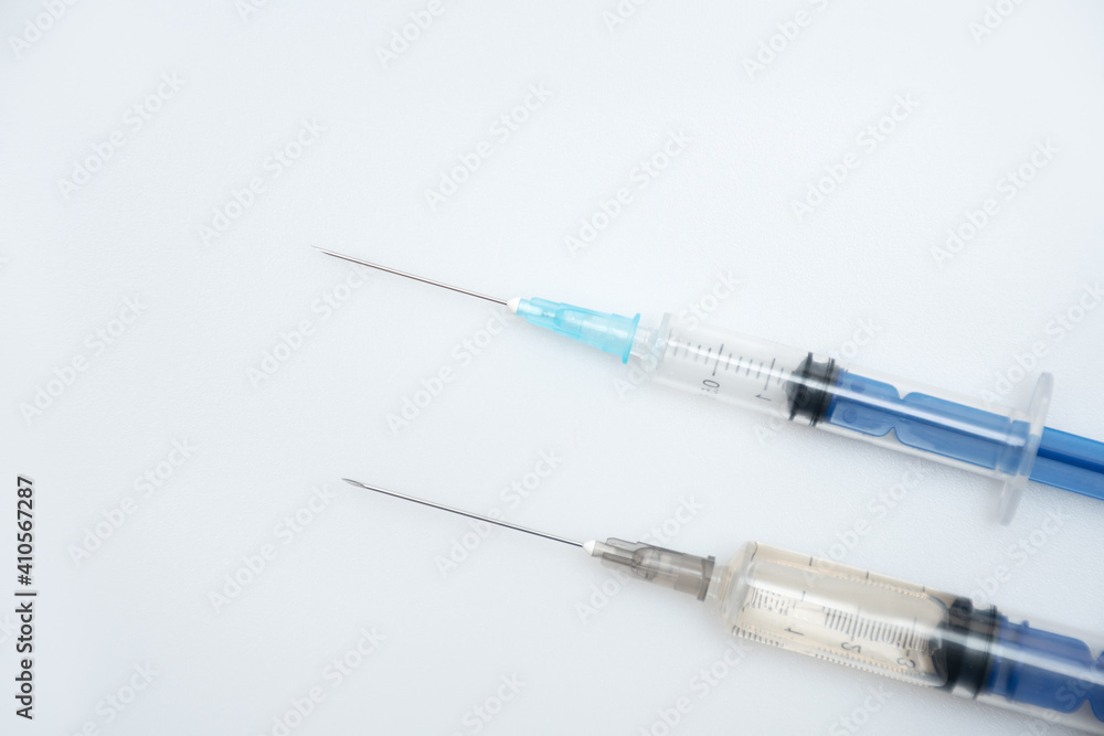 Two crossed syringes with a drug or vaccine lie parallel to each other on a white or gray background with space for text: coronavirus vaccination, top view Two crossed syringes with a drug or vaccine lie parallel to each other on a white or gray background with space for text: coronavirus vaccination, top view