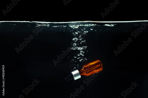 Bottle of cosmetic serum in clean transparent water in dark