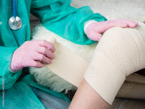 A physiotherapist applies an elastic bandage to the patient's injured knee.