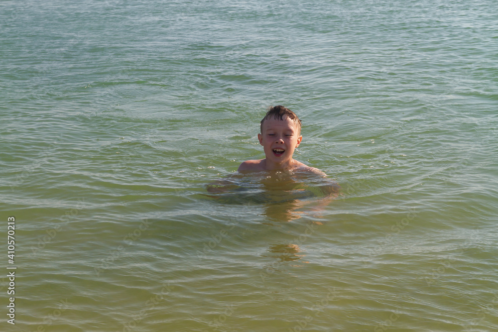 A teenage boy swims in the sea, lake or river with greenish water. The face of a teenager in water drops.