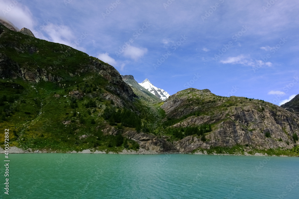 highest mountain with a sharp peak and snow between other mountains and a lake highest mountain with a sharp peak and snow between other mountains and a lake