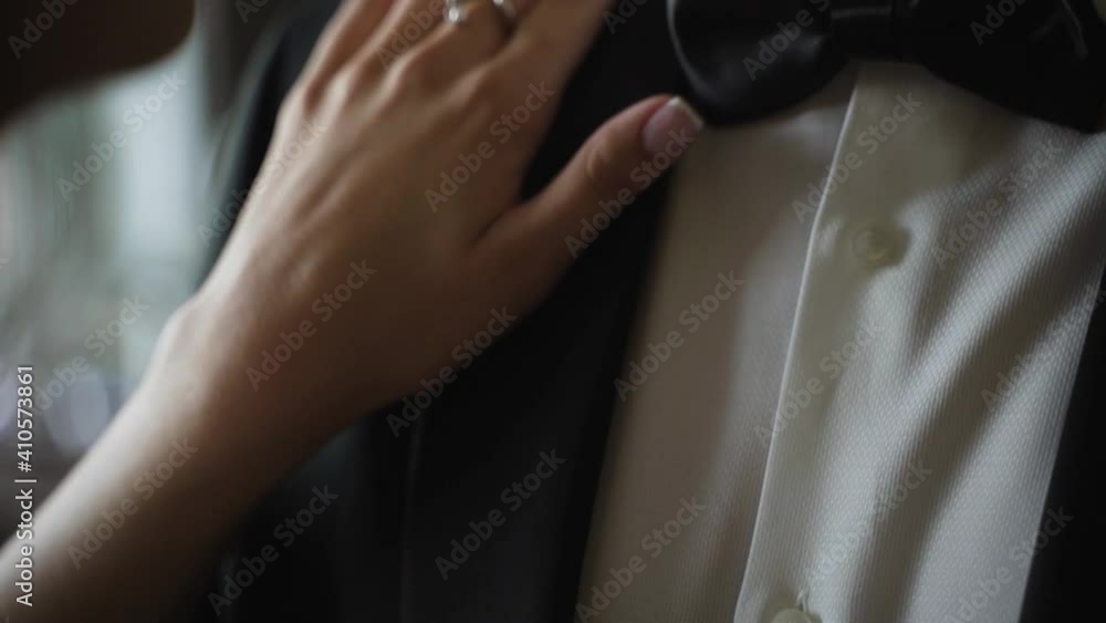 Bride touches groom's jacket. Bride and groom embrace. Groom in black classic suit and white shirt and bow tie Bride touches groom's jacket. Bride and groom embrace. Groom in black classic suit and white shirt and bow tie