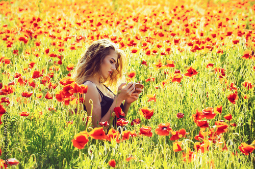 Beautiful teenager girl in blossom park. Woman in field of poppy making selfie photo.
